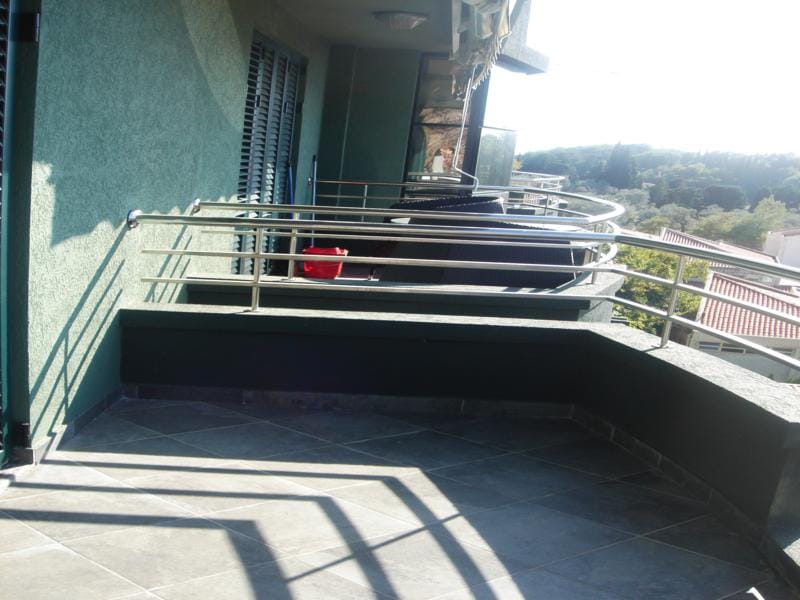 Spacious balcony with tile flooring and metal railing in an apartment, Miločer, Montenegro, overlooking green hills.