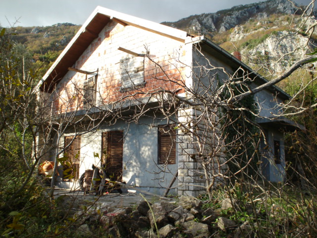 Two-story house for renovation on a plot in Herceg Novi, Montenegro, against a mountain backdrop.