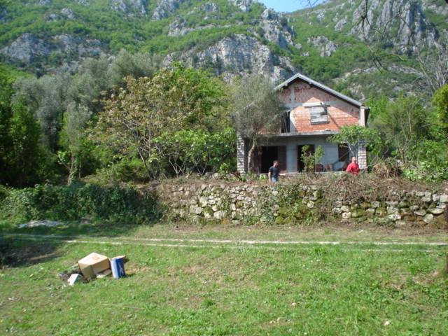 Two-story unfinished brick house on a plot of land in Herceg Novi, Montenegro, with mountains and greenery in the background.