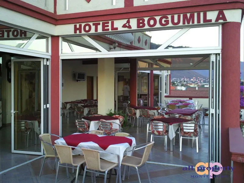 Open hotel terrace with set tables and chairs, overlooking a town and mountains.
