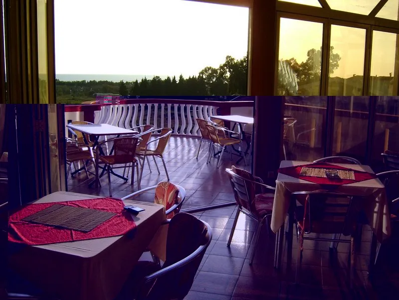 Tables and chairs on a terrace overlooking the sea, resembling an outdoor cafe or hotel lounge area.