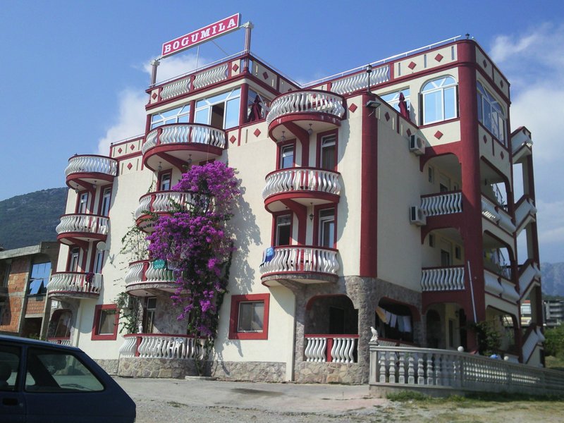 Facade of the Bogumila hotel in Bar, Montenegro: a four-story building with semicircular balconies and blooming bougainvillea.