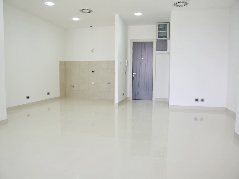 Bright office space in Budva, Montenegro: white walls, porcelain tile flooring, and a kitchen area, view of the entrance door.