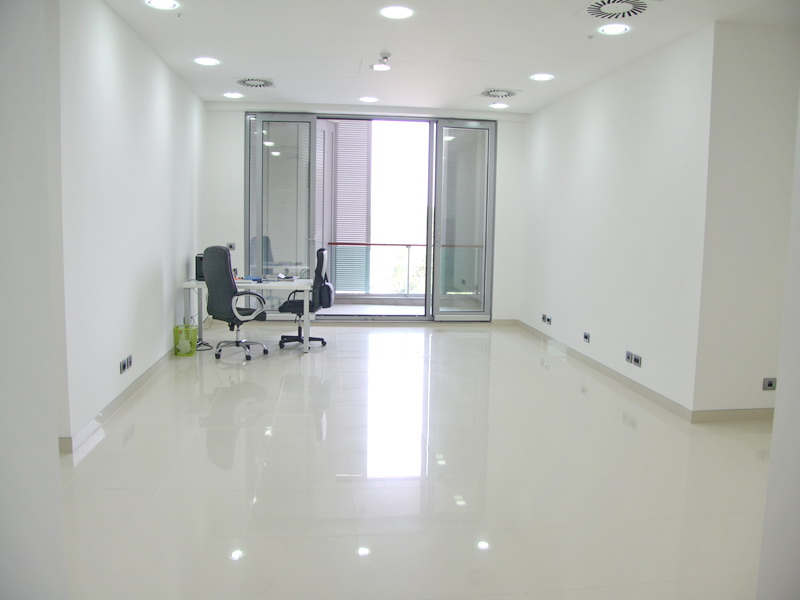 Bright office room in Budva, Montenegro: glossy floor, panoramic windows with access to the balcony, and office furniture.