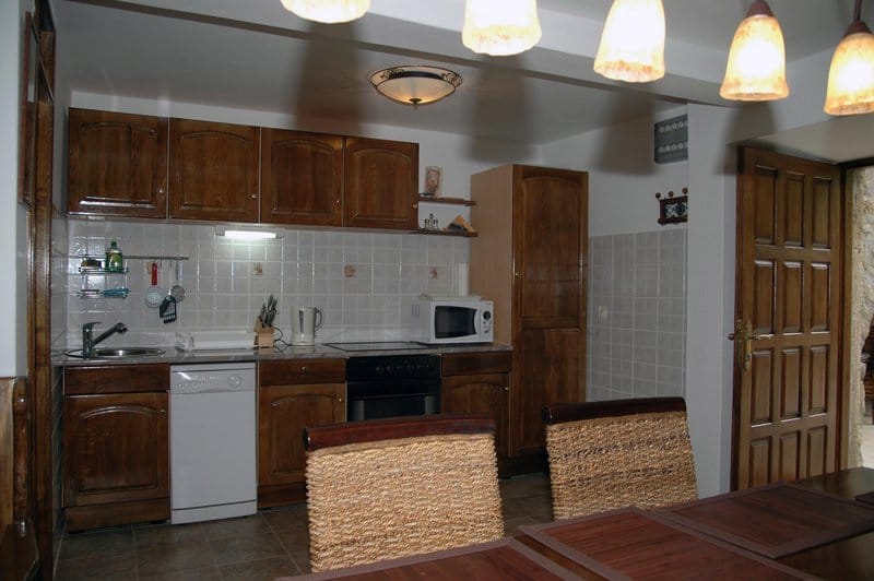 Kitchen with wooden cabinetry in a house in Rafailovici, Montenegro: built-in appliances, tile, and dining area.