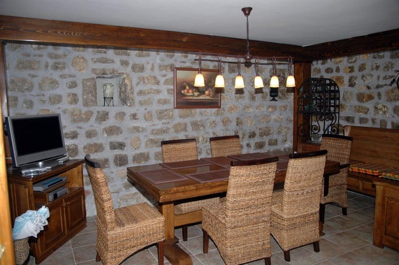 Living room with stone walls and wooden furniture in a house, Rafailovici, Montenegro. Dining area with wicker chairs.