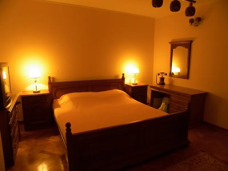 Bedroom featuring a wooden bed, nightstands, lamps, and a mirror under warm orange lighting.
