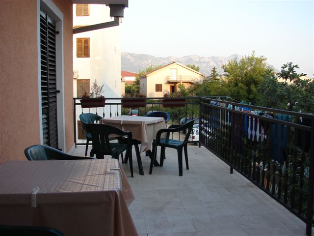 Spacious balcony with plastic furniture in a building in Budva, Montenegro, overlooking the mountains and neighboring buildings.