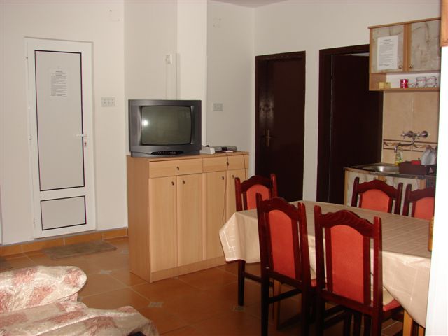 Living room with dining area and kitchen in a house in Budva, Montenegro: wooden table, chairs, and TV stand.