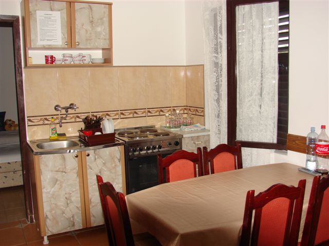 Kitchen with dining area in a house in Budva, Montenegro: stove, sink, wooden table, and chairs with red upholstery.