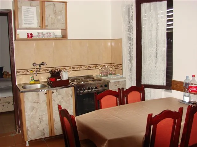 Kitchen with sink, stove, cabinets, and dining table with red chairs visible.