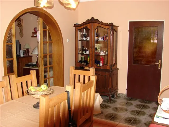 Dining area with wooden table, chairs, and a display cabinet near an arched doorway.
