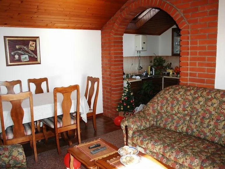 Living room with floral sofa and dining table, kitchen visible through brick arch.