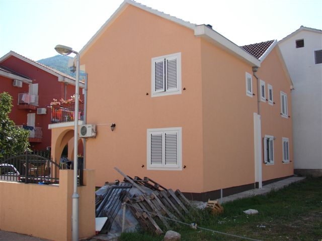 Two-story peach-colored house with white shutters on the windows in Budva, Montenegro, exterior view of the property.