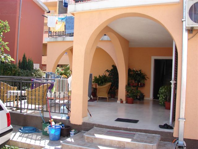 Cozy terrace with arches and wicker furniture by the house in Budva, Montenegro. View of the yard and the house entrance.