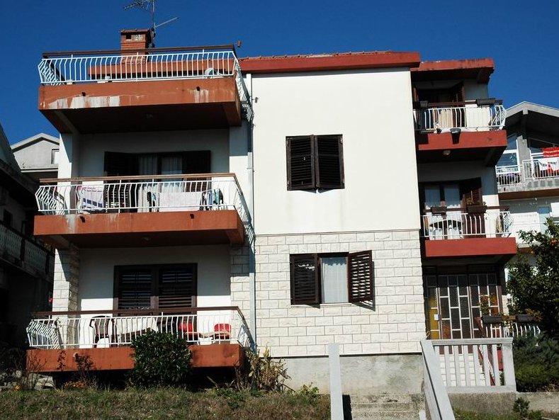 Three-story house in Herceg Novi, Montenegro: facade with terraces, stone cladding, and wooden shutters on the windows.