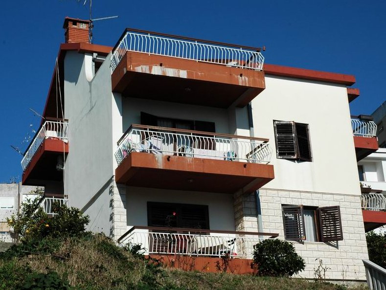 Three-story house in Herceg Novi, Montenegro: facade with terraces, white trim, and a stone base against the sky.