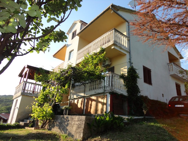 Three-story house in Herceg Novi, Montenegro, with terraces, balustrades, grapevine, and a garden in front of the facade.