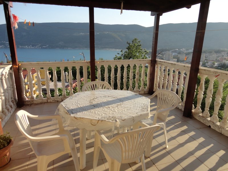 Terrace with sea and mountain views in a house in Herceg Novi, Montenegro: plastic furniture, balustrade, and awning.