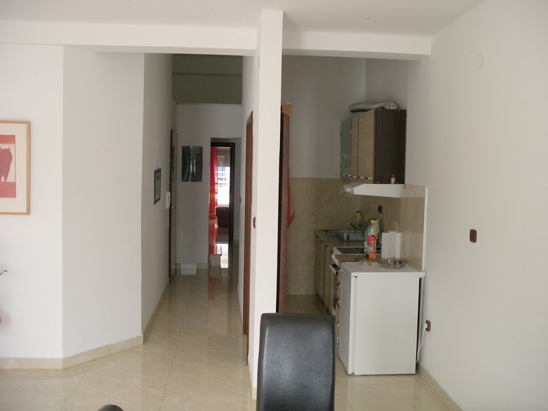 Apartment interior in Rafailovici, Montenegro: a compact kitchen with white cabinetry and a hallway with tiled flooring.