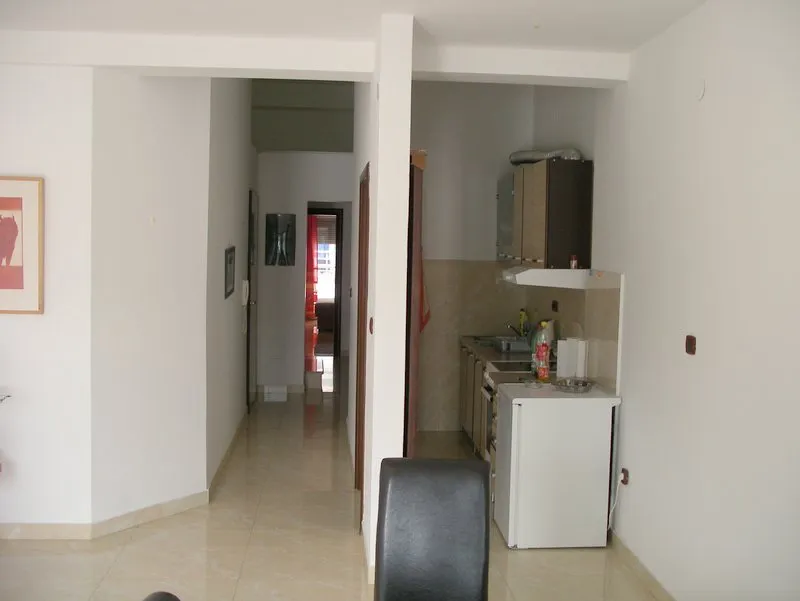 Open kitchen area with cabinets, sink, hood, and mini-fridge visible next to a hallway.