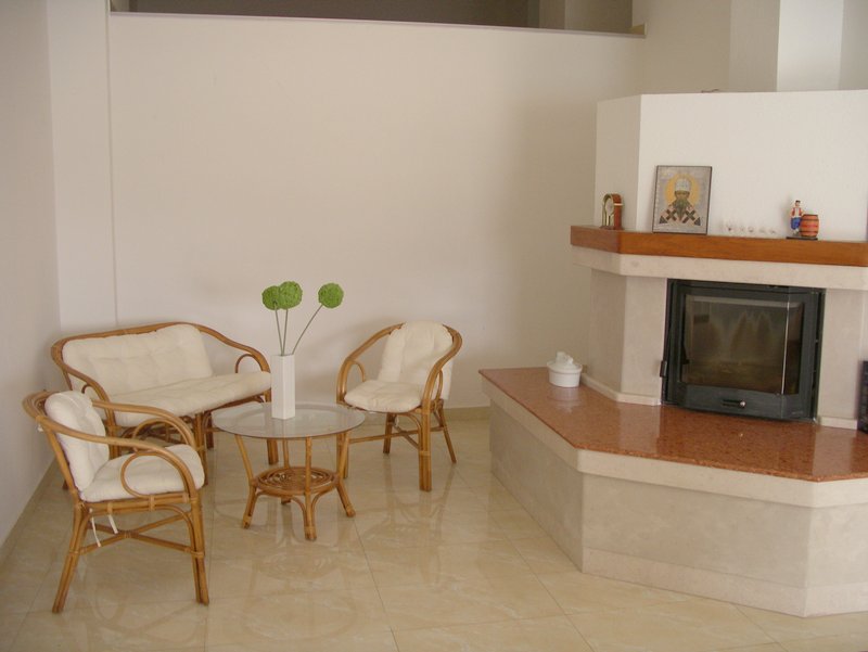 Living room with a fireplace and wicker furniture in an apartment in Rafailovici, Montenegro: bright interior with tiled flooring.