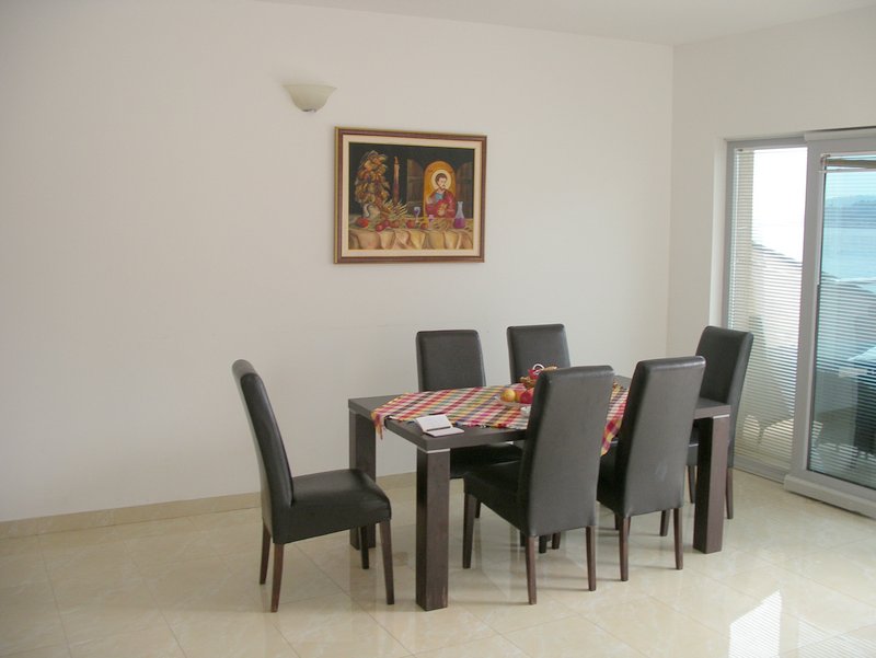 Bright living room with dining area in an apartment, Rafailovici, Montenegro: dark table, chairs, and sea view from the window.