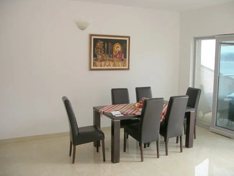 Dining area with a dark wood table, six black chairs, and a religious painting on a white wall next to glass doors.