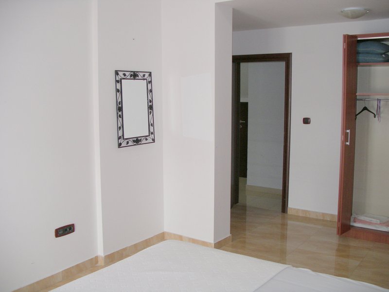 Bedroom interior in an apartment in Rafailovici, Montenegro: white walls, a mirror in a wrought-iron frame, and a built-in wardrobe.