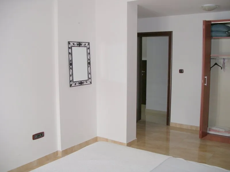 Bedroom featuring a mattress, wall mirror, and open wooden wardrobe with hangers visible.