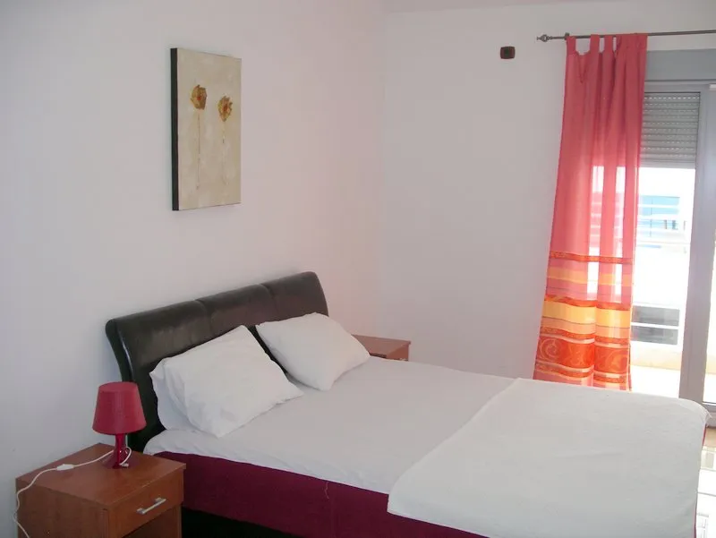 Bedroom with double bed, wooden nightstand, red lamp, and pink curtains.