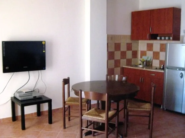 Kitchen area with wooden cabinets, fridge, dining table, and wall-mounted TV.