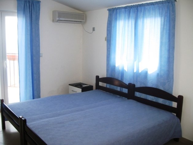 Bedroom with a double bed and air conditioning in a villa in Budva, Montenegro: bright interior with blue curtains.
