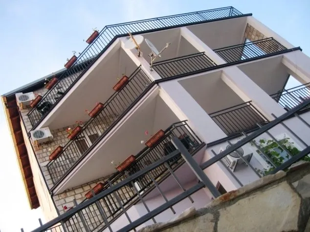 Low-angle view of a building facade featuring multiple balconies with black railings and AC units.