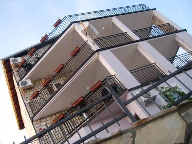 Three-story villa in Budva, Montenegro: bottom-up view of the building with stone cladding and open balconies with railings.