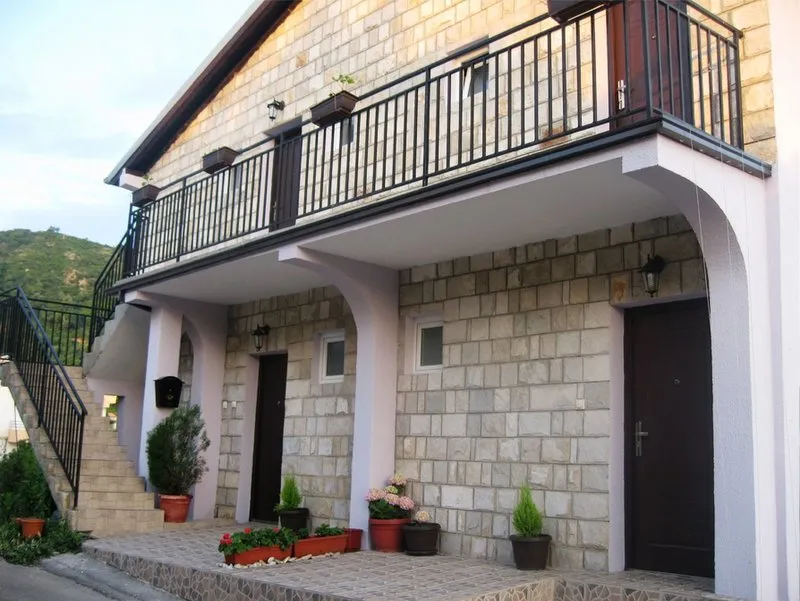 Stone house facade featuring a balcony, exterior staircase, and potted plants near the entrance.