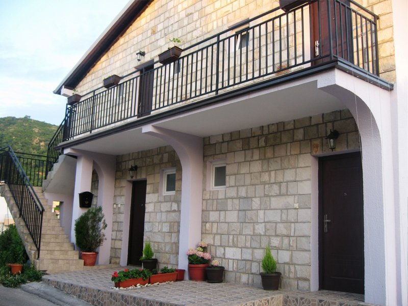 Facade of a two-story villa in Budva, Montenegro: stone cladding, open terrace, balcony, and exterior staircase.