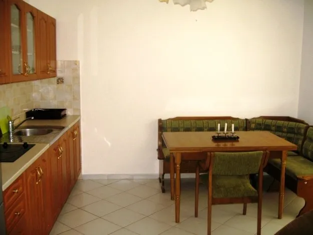 Kitchen with wooden cabinets, sink, stove, and dining area featuring a green sofa and wooden table.