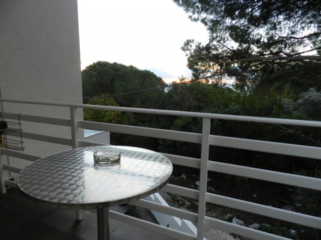 View from the balcony of a house in Bar, Montenegro: a metal table and a panoramic view of a green garden and trees.