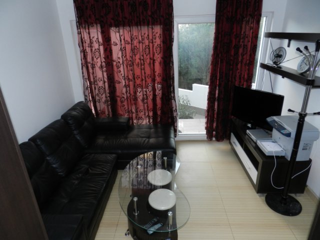 Living room with a black leather sofa and glass table in a house in Bar, Montenegro, with a view of the terrace and garden.