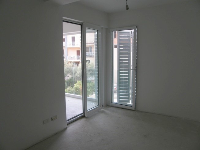 Bright living room in a new building in Pržno, Montenegro: white walls, panoramic windows with blinds, and access to the terrace.