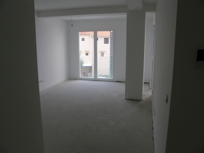 Bright living room in a new building in Pržno, Montenegro: finished interior, panoramic window, and view of neighboring houses.
