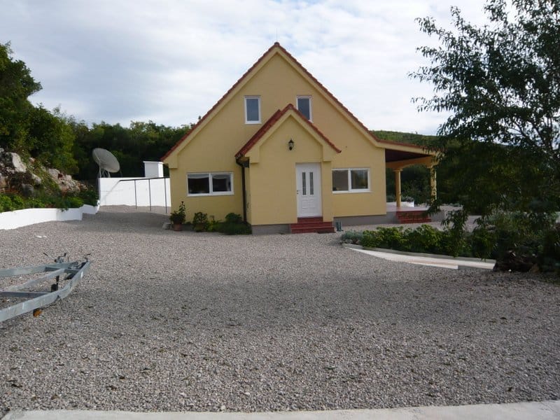 Two-story yellow private house with a terrace and gravel yard in Nikšić, Montenegro.