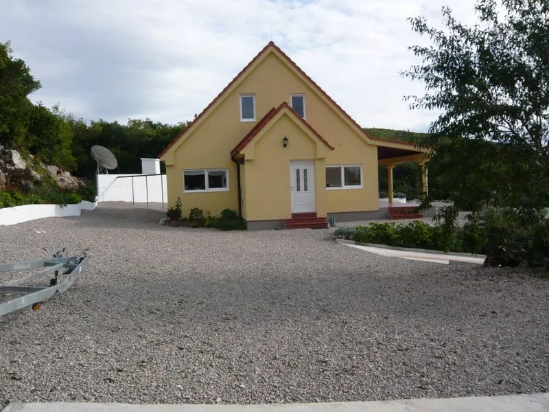 Yellow house with red roof and gravel driveway, exterior view.