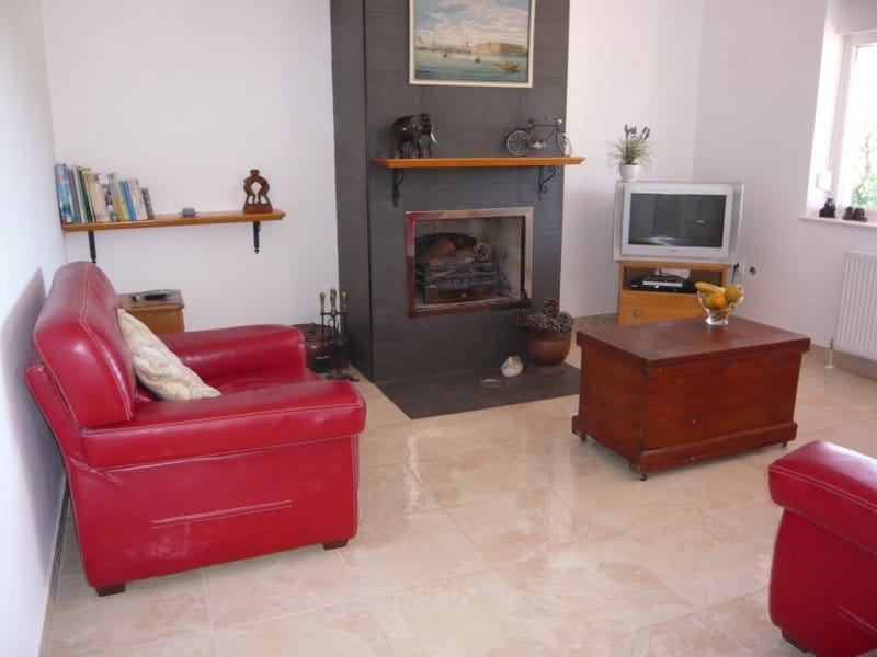 Living room in a house in Nikšić, Montenegro: red leather armchairs, a fireplace with dark trim, and a light tiled floor.