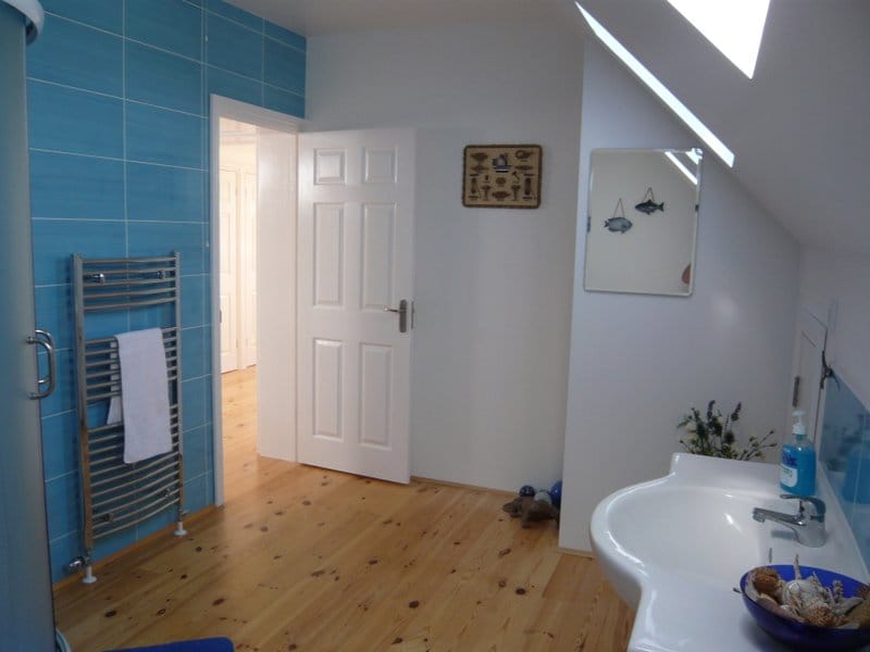 Bright bathroom in a house in Nikšić, Montenegro: wooden floor, blue tiles, sink, and skylight.