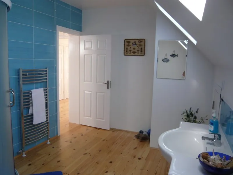 Bathroom with blue tiles, heated towel rail, white sink, wooden floor, and skylight under a sloped ceiling.