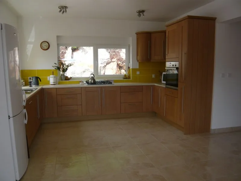 Kitchen with wooden cabinets, white fridge, stove, and yellow backsplash under a window overlooking rocks.