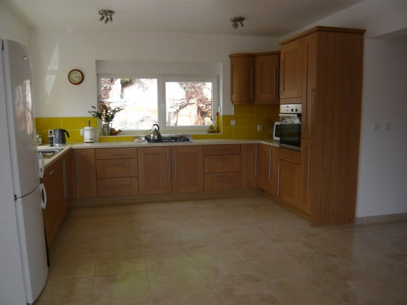 Spacious kitchen with wooden cabinets and a yellow backsplash in a house for sale, Nikšić, Montenegro.