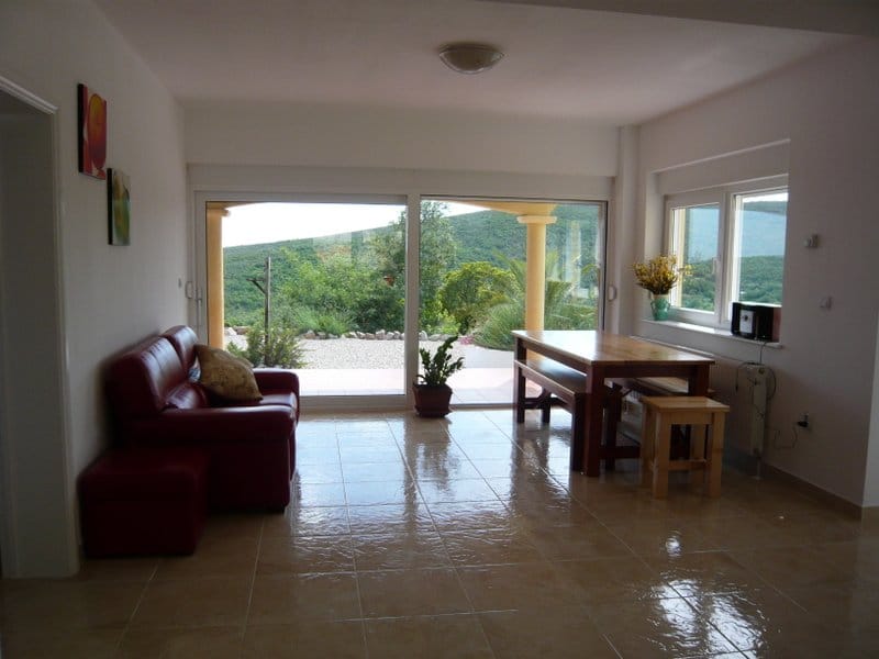 Living room in a house in Nikšić, Montenegro: red sofa, wooden table, panoramic windows with a view of the mountains and terrace.